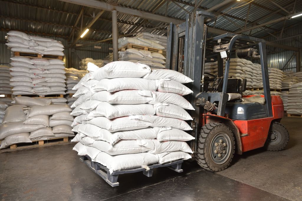 Chariot élévateur portant une palette de sacs de grain dans un entrepôt où d'autres sacs sont empilés sur palettes